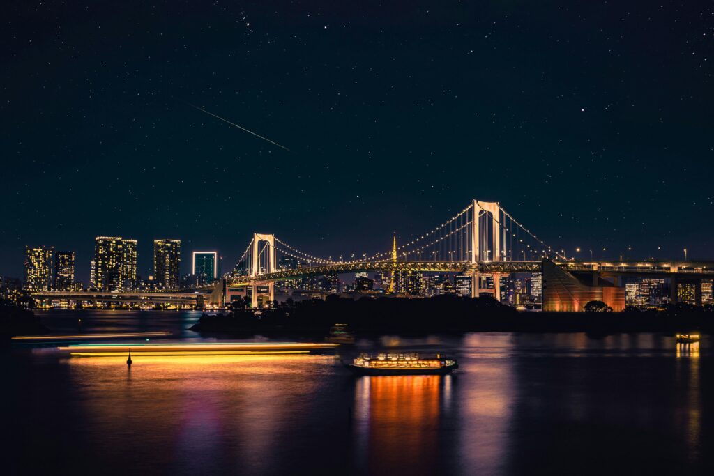 Night view of Tokyo's Rainbow Bridge under a starry sky, reflecting city lights on the water.